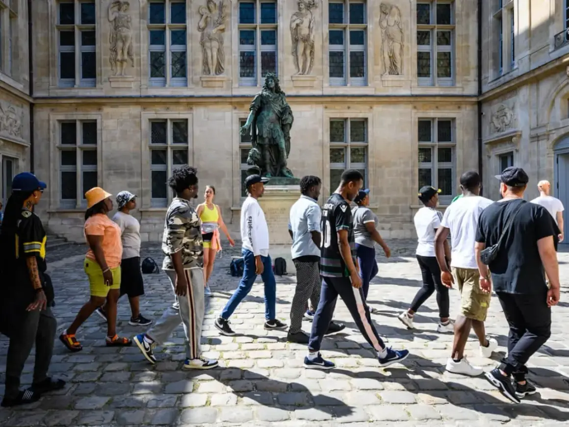 Un groupe de jeunes explore les musées de Paris, admirant une statue devant un bâtiment historique.