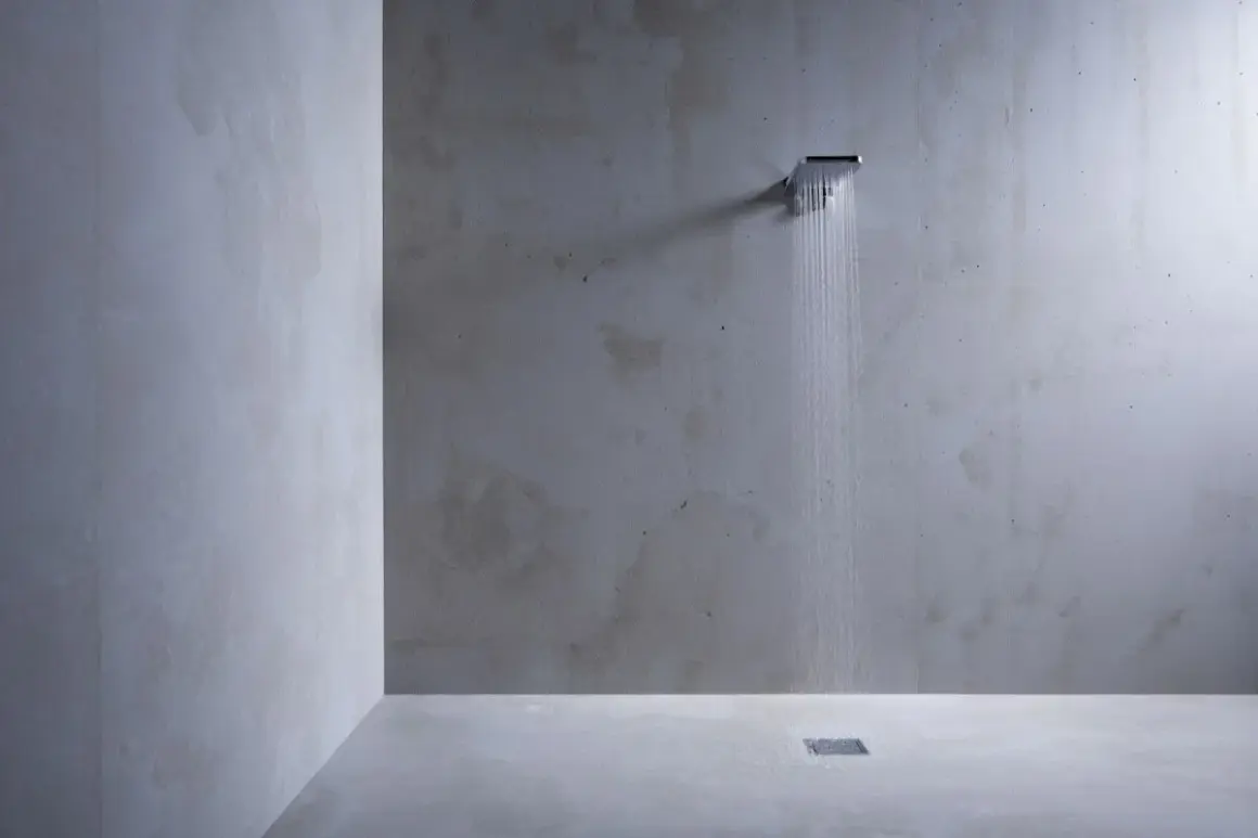 Douche moderne au design épuré, avec un mur et un sol en béton ciré. L'eau coule d'une douchette carrée, créant une ambiance zen.