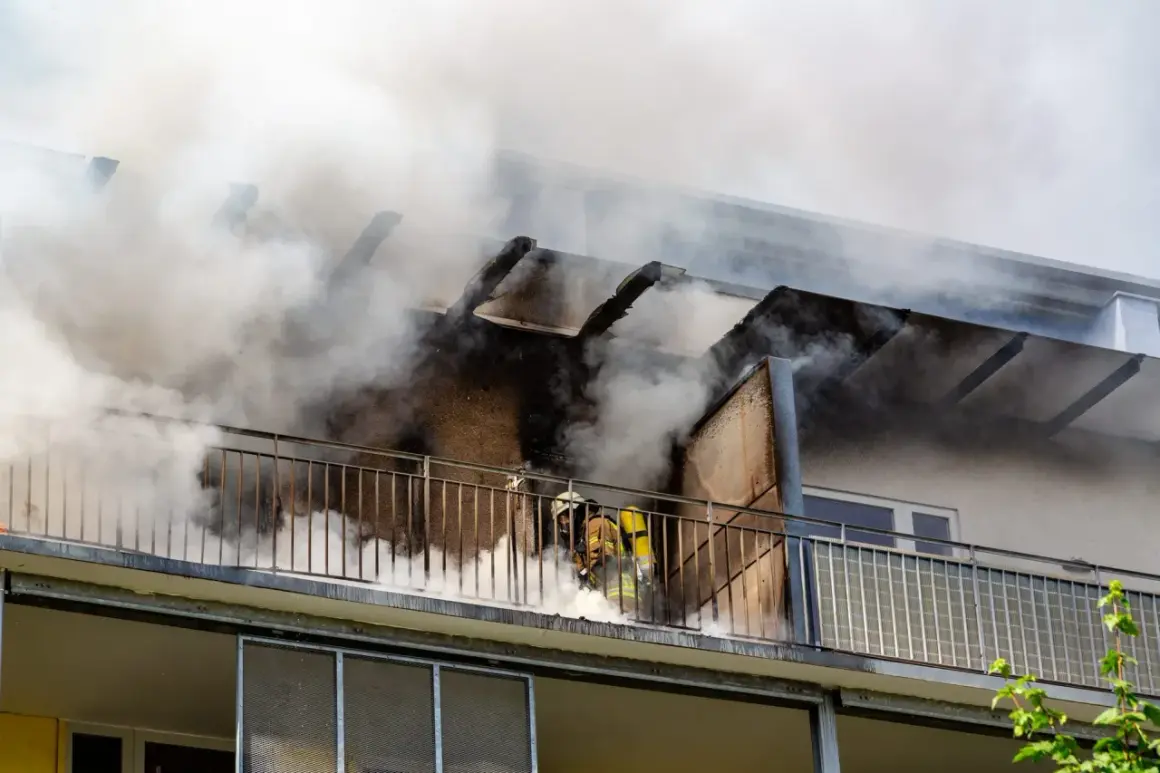 Feuerwehrleute kämpfen gegen einen Wohnungsbrand. Rauch quillt aus dem Gebäude. Ein Albtraum ohne Hausratversicherung.