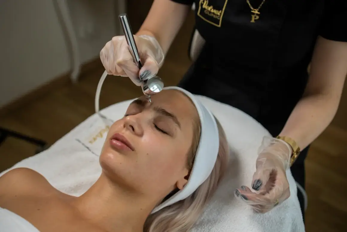 Zabieg dermaoxy na twarz młodej kobiety. Kosmetolog wykonuje zabieg urządzeniem, które rozpyla strumień tlenu i substancji aktywnych.
