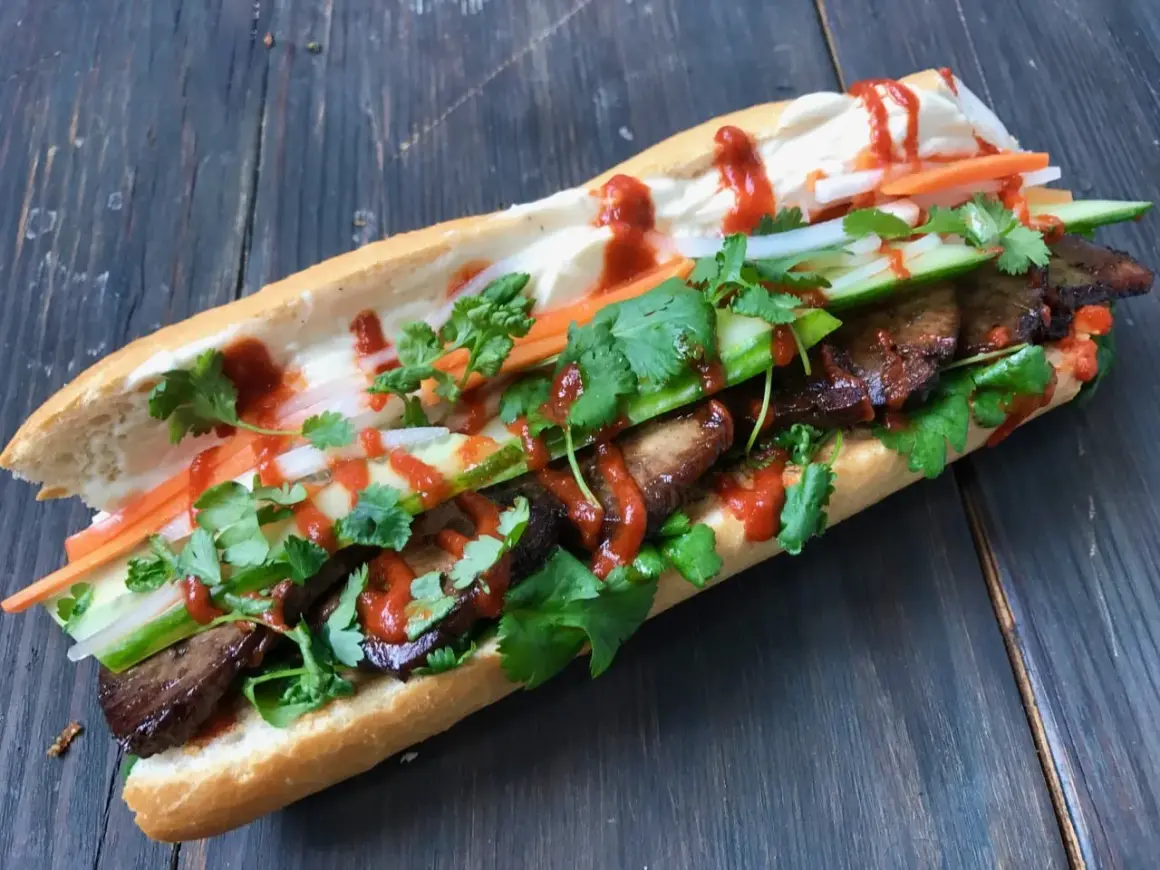 En saftig banh mi med tofu, färska grönsaker och en härlig sås på en träbakgrund.