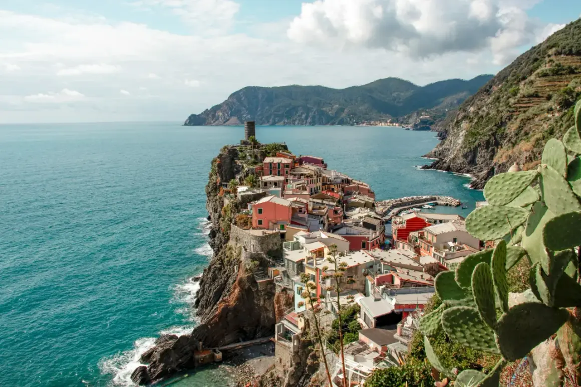 Pueblo costero de casas coloridas en un acantilado, con el mar azul y montañas al fondo. Un lugar que evoca la esencia de la spezia el ejido.