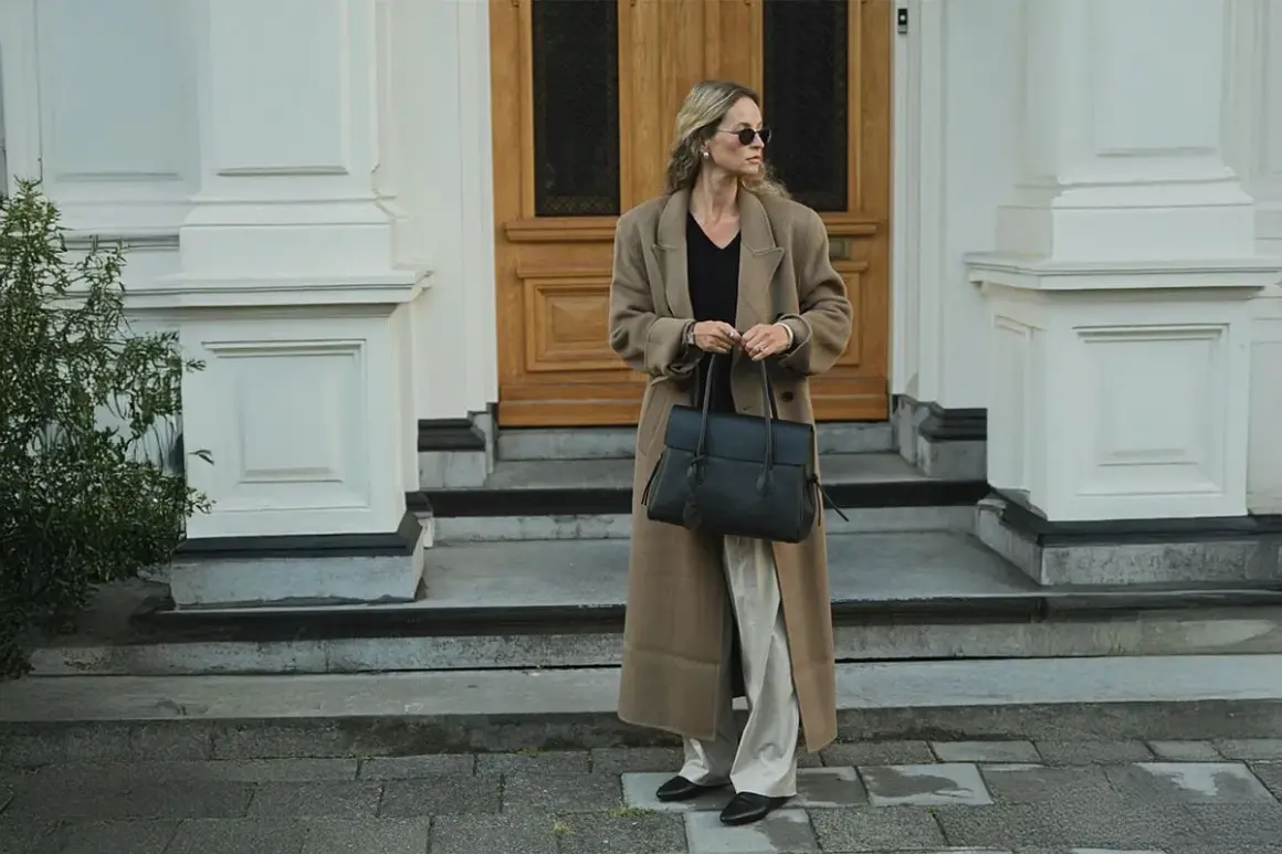 En kvinna med solglasögon bär en elegant brun kappa och håller en stilren vero moda väska.