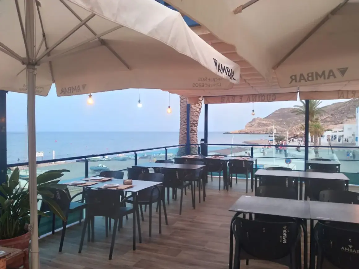 Terraza de restaurante con mesas y sillas, vistas al mar y a la playa. Un lugar ideal para disfrutar de un socorrito las negras al atardecer.