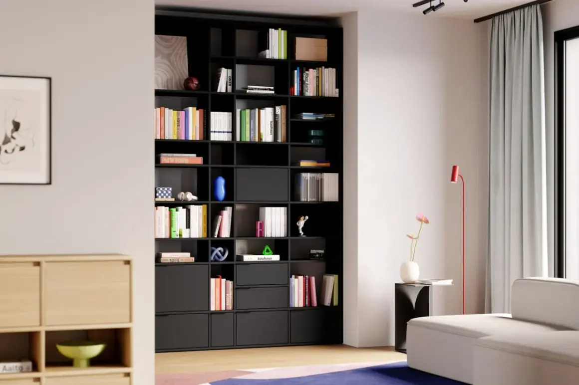 Moderne studio einrichtung mit schwarzem Regal voller Bücher und Deko-Objekte. Ein helles Sofa und ein roter Stehlampen ergänzen den Raum.