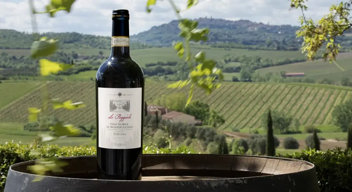 Bottiglia di vino nobile di Montepulciano DOCG su un barile, con vigneti e colline toscane sullo sfondo.
