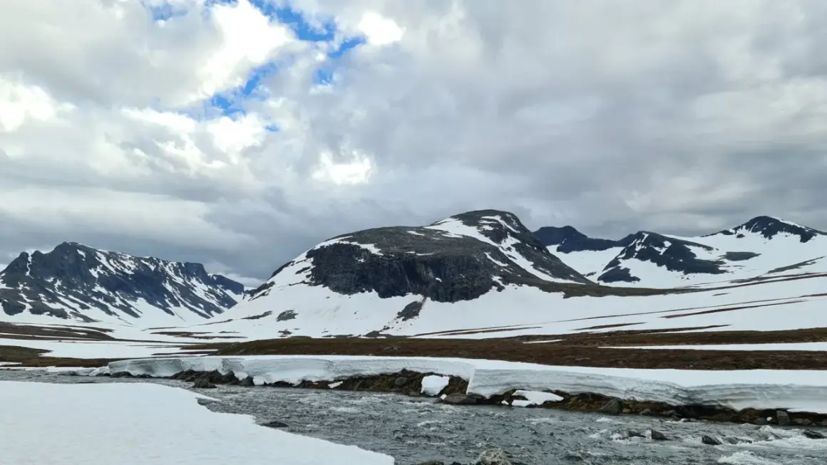 Snöklädda berg och en forsande älv i Jämtland, en vy som inspirerar till att bestiga Sylarna.