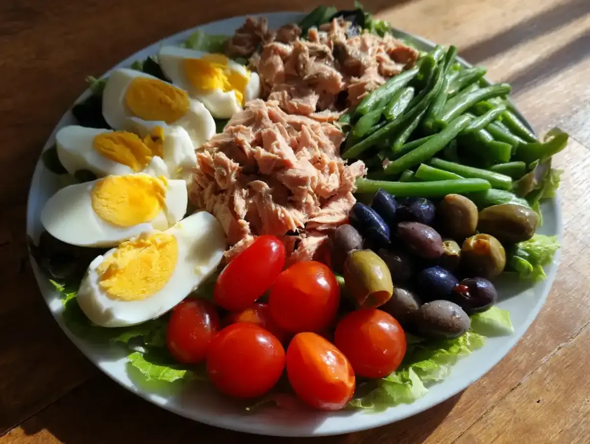 En härlig sallad nicoise med ägg, tonfisk, gröna bönor, tomater och oliver på en bädd av sallad.