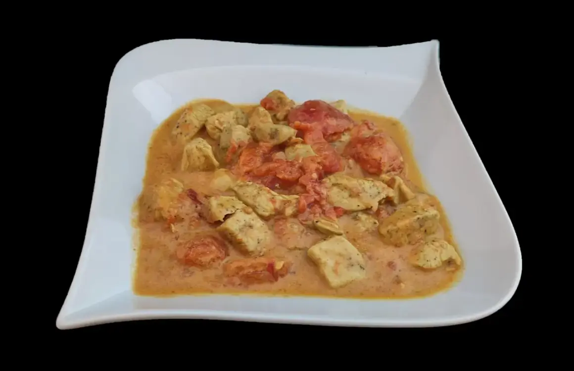 Un plat de poulet curry coco crémeux avec des morceaux de poulet tendre et des tomates, servi dans une assiette blanche.