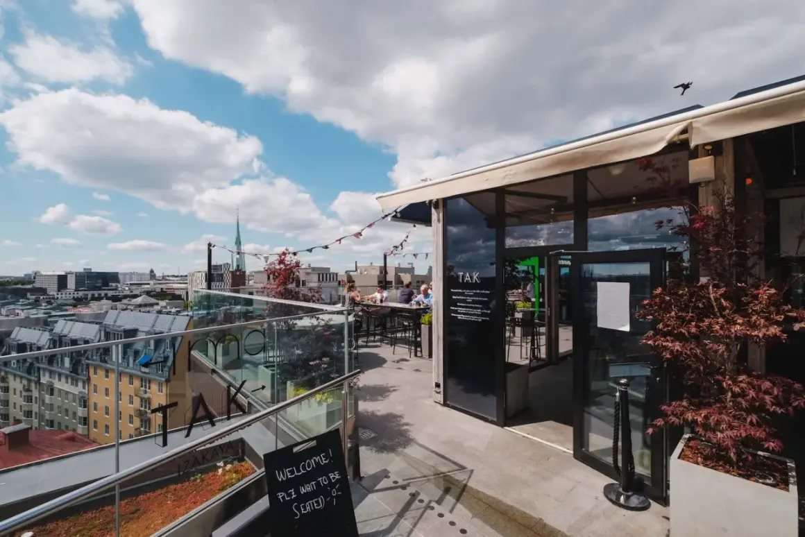 En takterrass med uteserveringar i Stockholm. Soliga moln på himlen, folk sitter vid borden och njuter av utsikten.