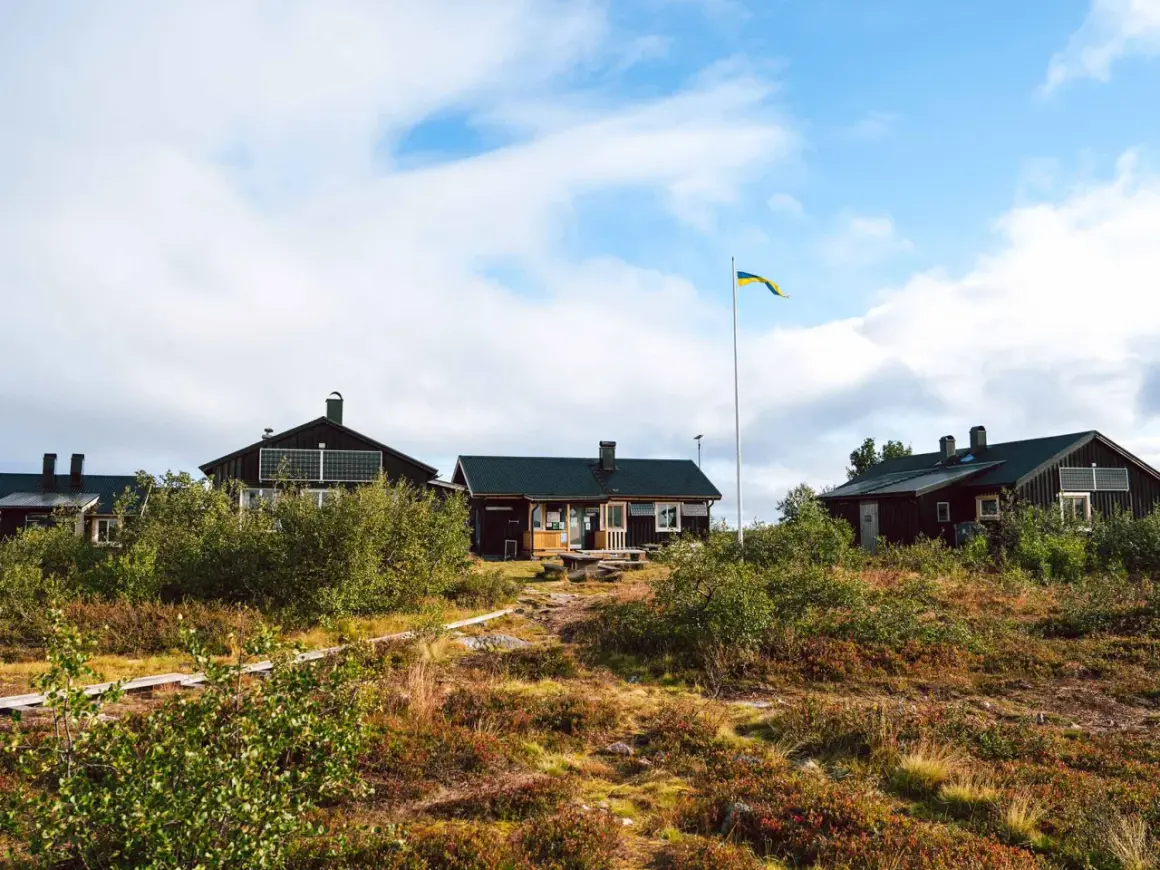 Mörka trähus med solpaneler och en svensk flagga som vajar vid ett vandrarhem i Dalarna.
