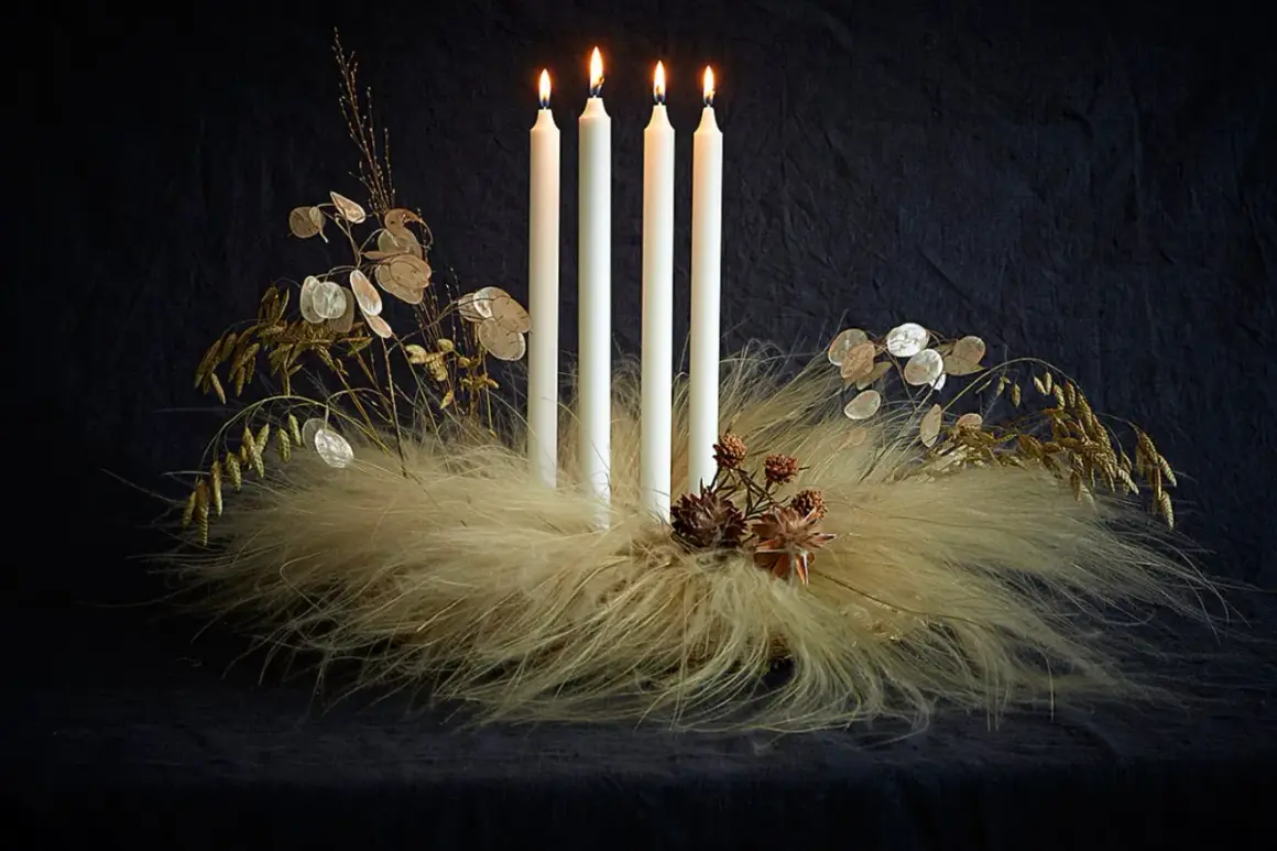Ausgefallener Adventskranz Trend: Vier weiße Kerzen auf einem Bett aus Federn und Gräsern, geschmückt mit Lunaria und Zapfen.