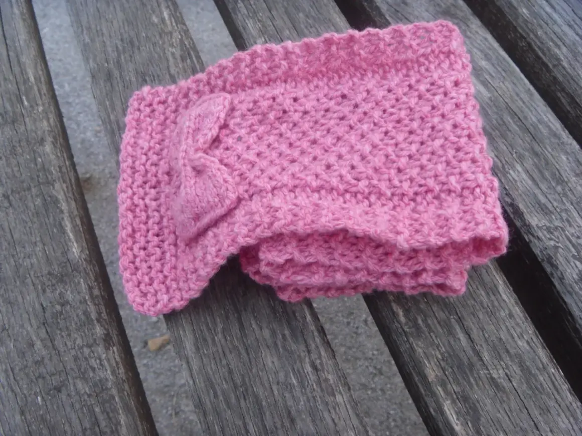 Sciarpa bimba ai ferri con fiocco, lavorata a maglia con schema semplice. Morbida e rosa, perfetta per l'inverno.