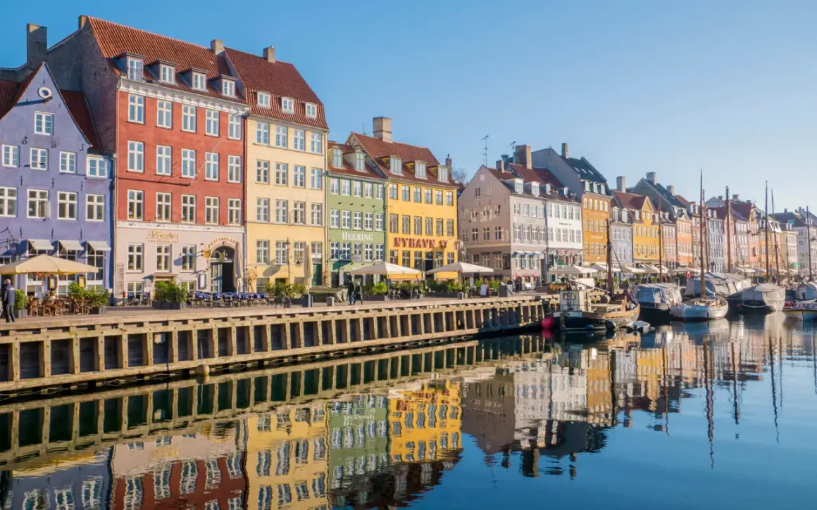 Kolorowe kamienice nad kanałem Nyhavn to obowiązkowy punkt na mapie kopenhaga co zobaczyć. Widać tu odbijające się w wodzie łodzie i budynki.