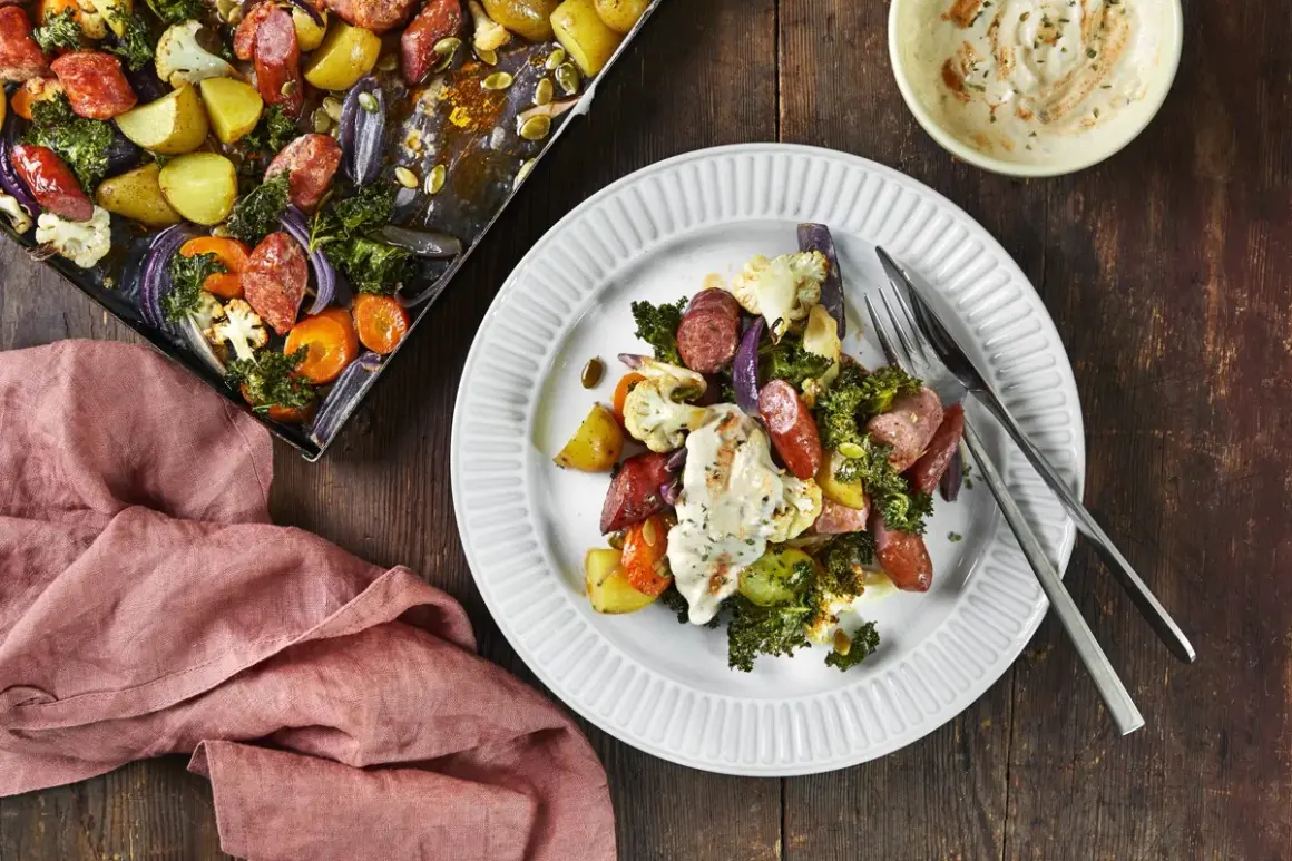 En tallrik med ugnsrostade grönsaker och korv, ett perfekt potatis recept. Bredvid syns en ugnsplåt med samma läckra innehåll.