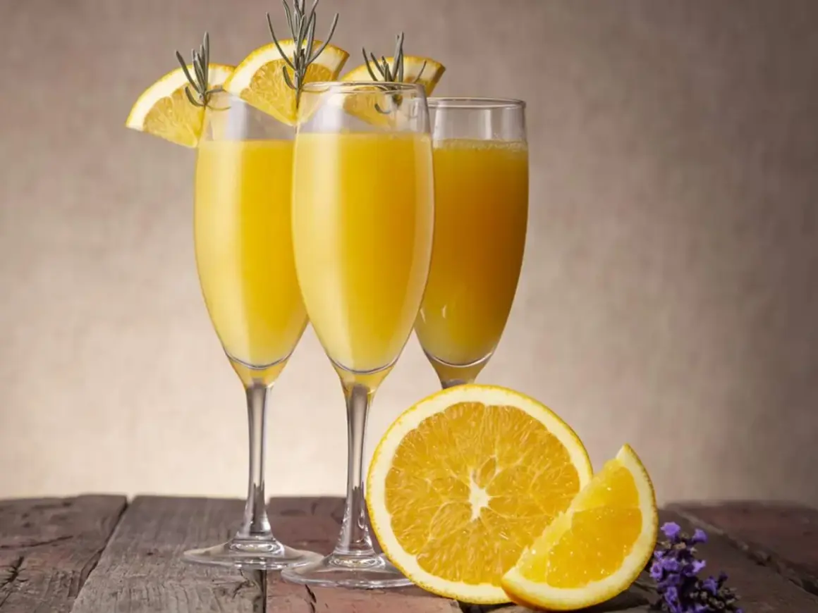 Tre glas med en gyllene drink med cava, garnerade med apelsinskivor och rosmarin. En apelsin och lavendel på träbordet.