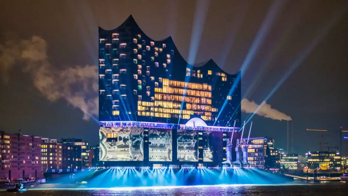 Elbphilharmonie, konserthus Hamburg, badar i ljus och strålkastare över vattnet en mörk kväll.