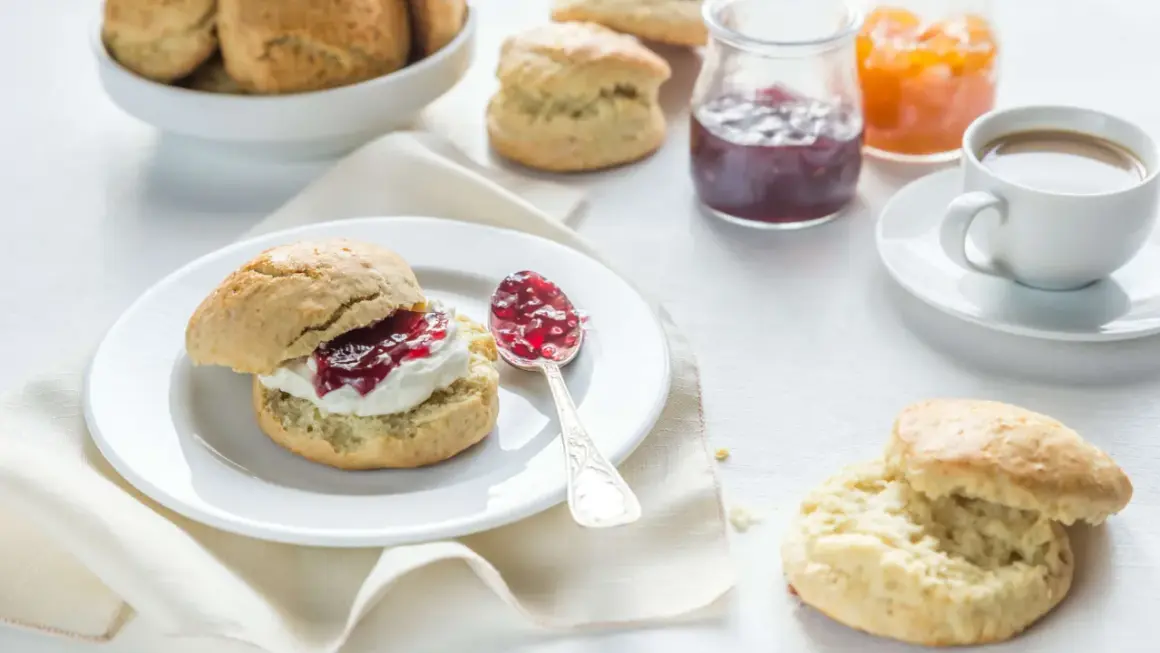 Ein Scone mit Clotted Cream und Marmelade, daneben eine Tasse Kaffee und weitere Scones.