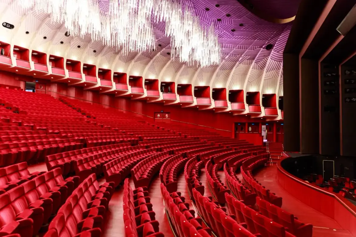 Interno di un teatro moderno con file di poltrone rosse e un soffitto decorato. Uno dei teatri più grandi d'Italia, pronto ad accogliere il pubblico.