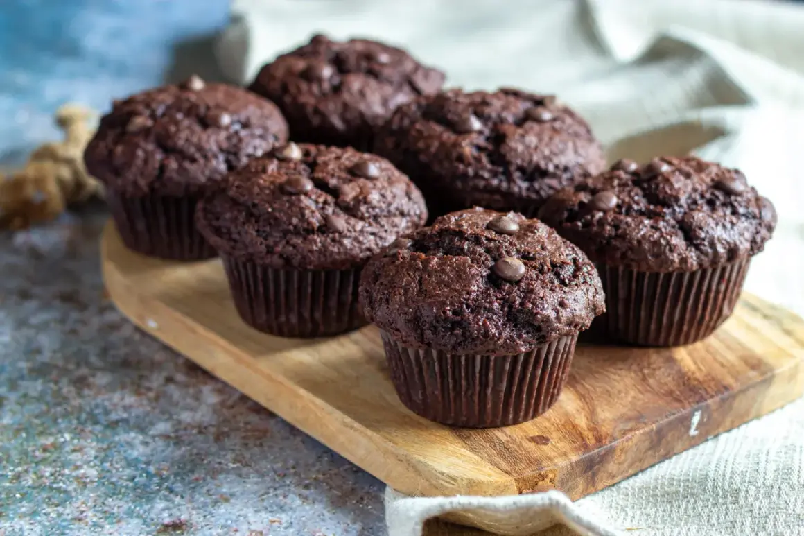 Muffins med chokladbitar, saftiga och mörka, ligger uppradade på en träbricka. Perfekta för fikat!