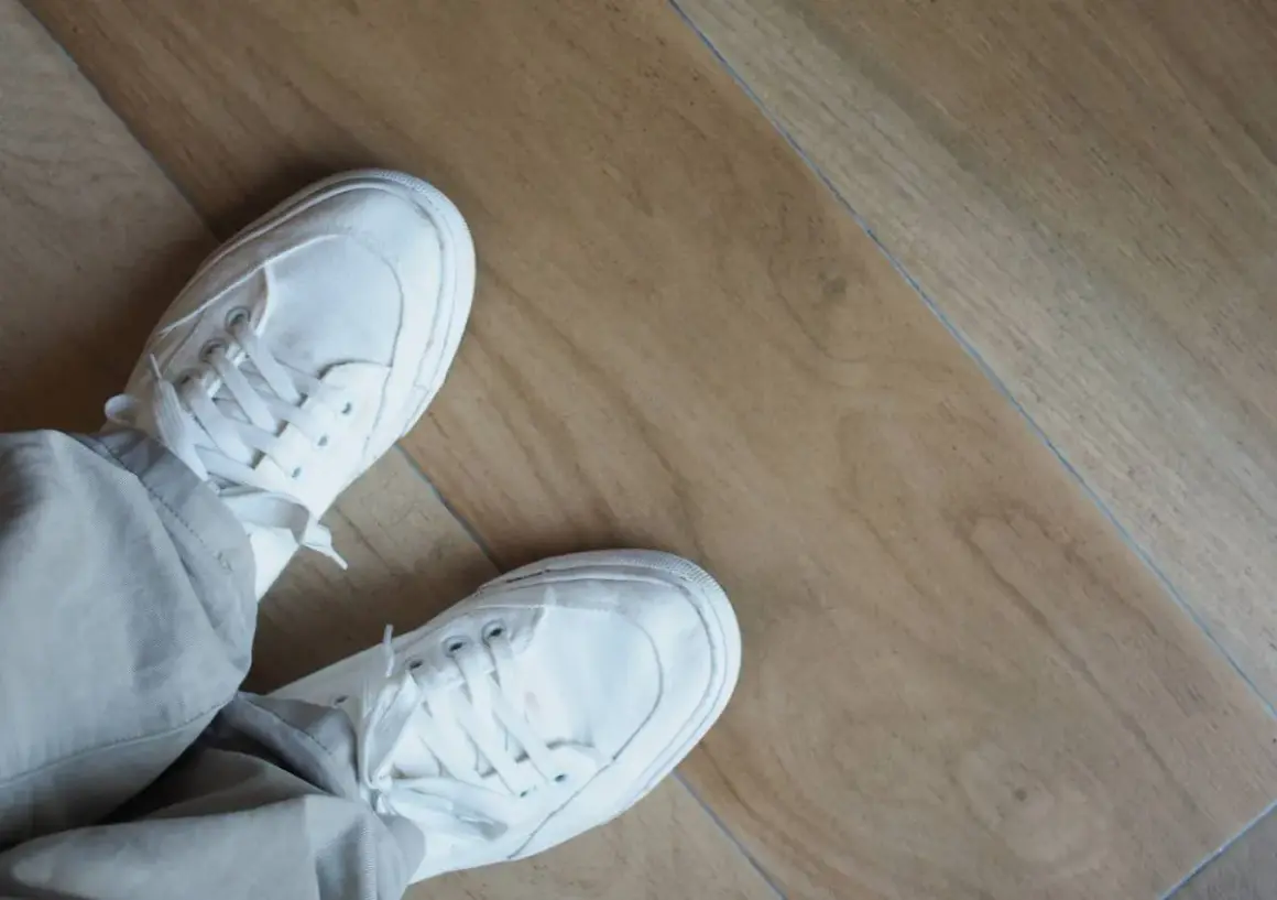 Piedi con scarpe bianche su un pavimento in laminato effetto legno. Questo pavimento spc cos'è? È un materiale resistente e moderno.