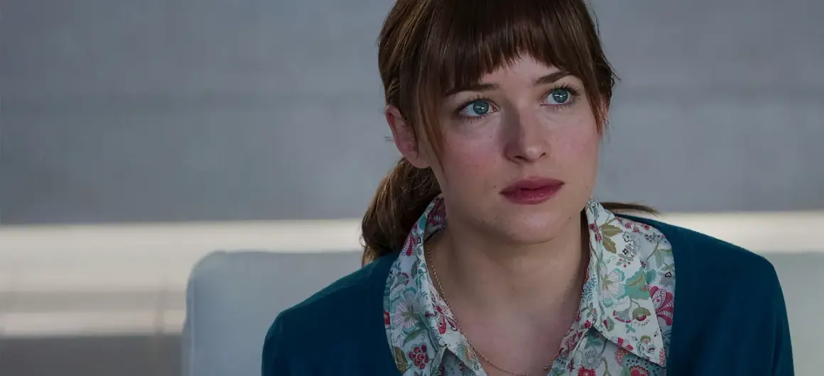 Dakota Johnson with blue eyes and brown hair, wearing a floral shirt and teal cardigan.
