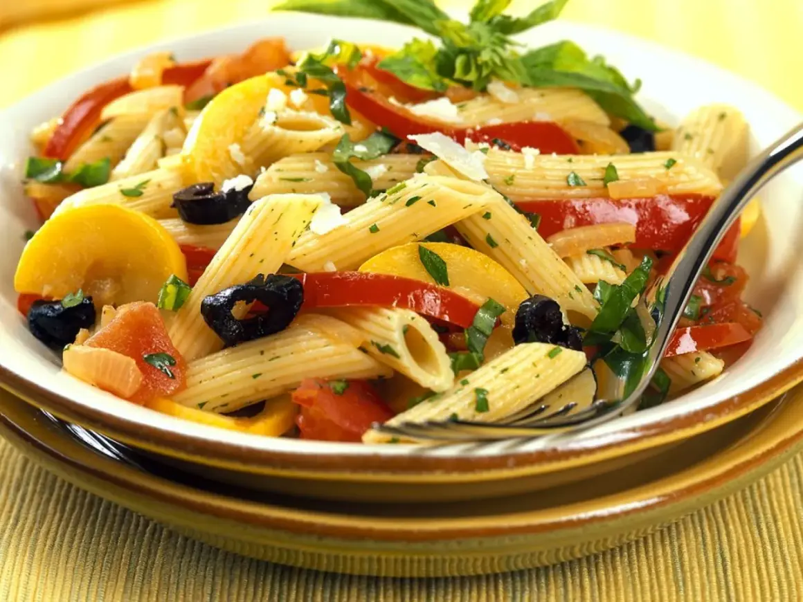 Bunte Nudelgerichte mit Penne, Tomaten, Zucchini, schwarzen Oliven und frischen Kräutern, garniert mit Parmesan.