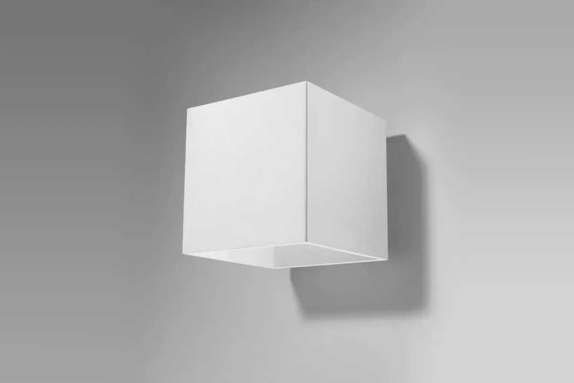 Minimalistyczna lampa kostka w kolorze białym, zamontowana na szarej ścianie. Rzuca subtelny cień.