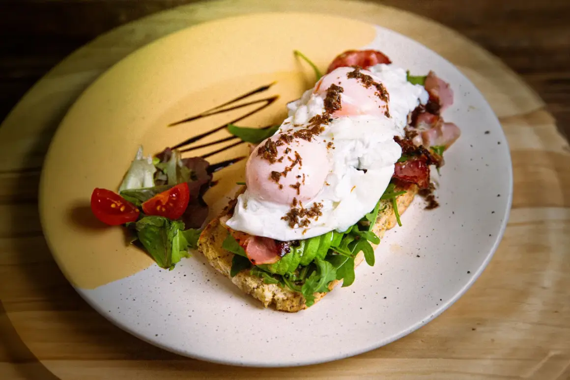 Tostada con aguacate, huevo escalfado y bacon, perfecta para un all day brunch. Acompañada de tomates cherry y rúcula.