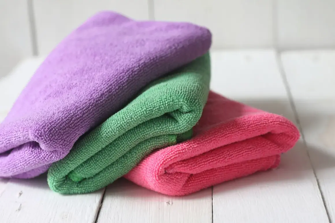 Drei bunte Mikrofasertücher, lila, grün und pink, liegen übereinander. Sie warten darauf, dass man sie zum putzlappen waschen benutzt.