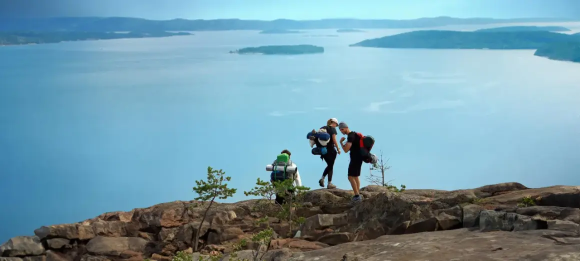 Vandrare med ryggsäckar njuter av utsikten över den blåa skärgården vid Höga kusten.