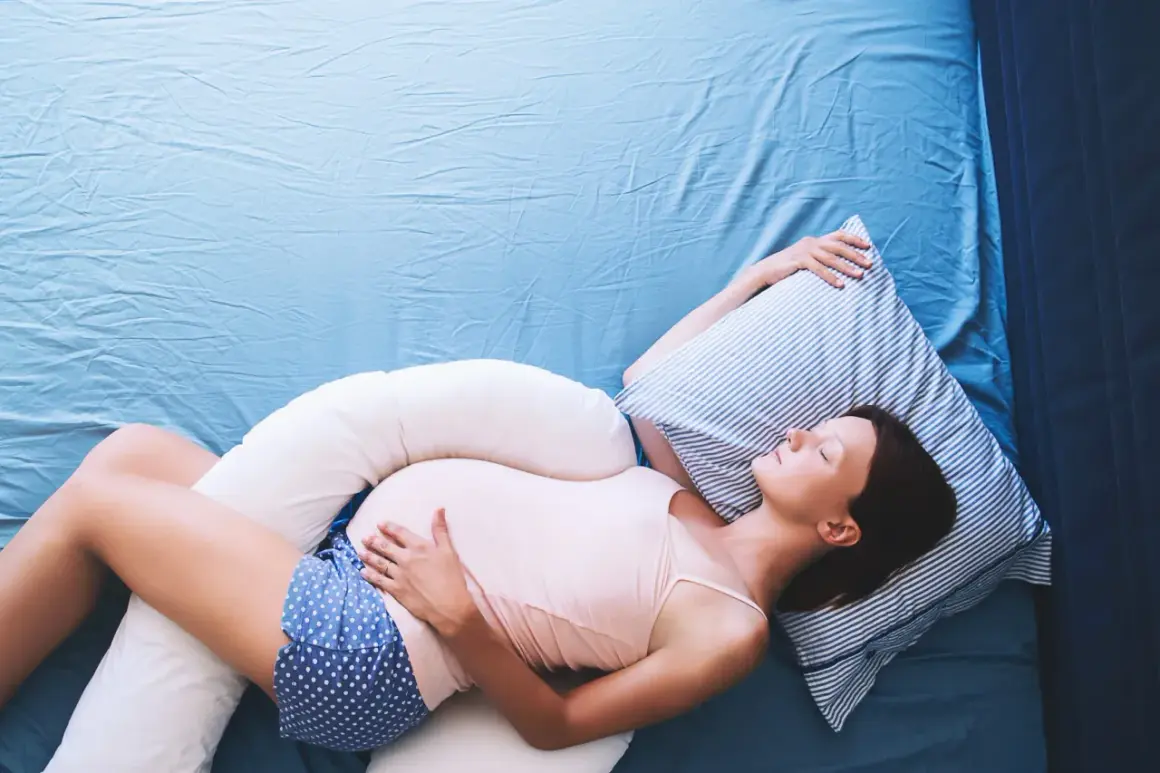 Mujer embarazada durmiendo de lado con almohadas de apoyo, una solución para como dormir con pubalgia y disfrutar del descanso.