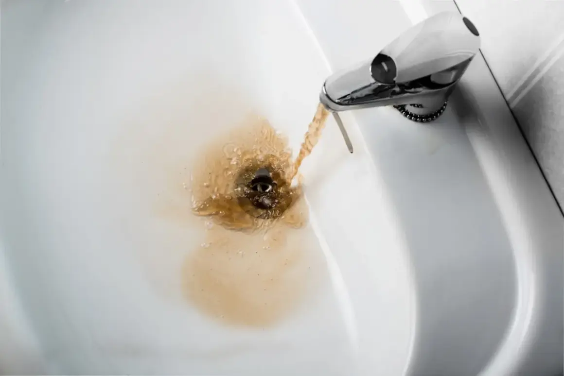 Acqua gialla dalla caldaia che scorre nel lavandino, creando un alone marrone.