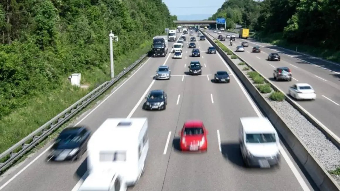 Autobahn mit vielen Autos und einem Wohnwagen. Ein Schild am Horizont deutet das ende autobahn schild an.