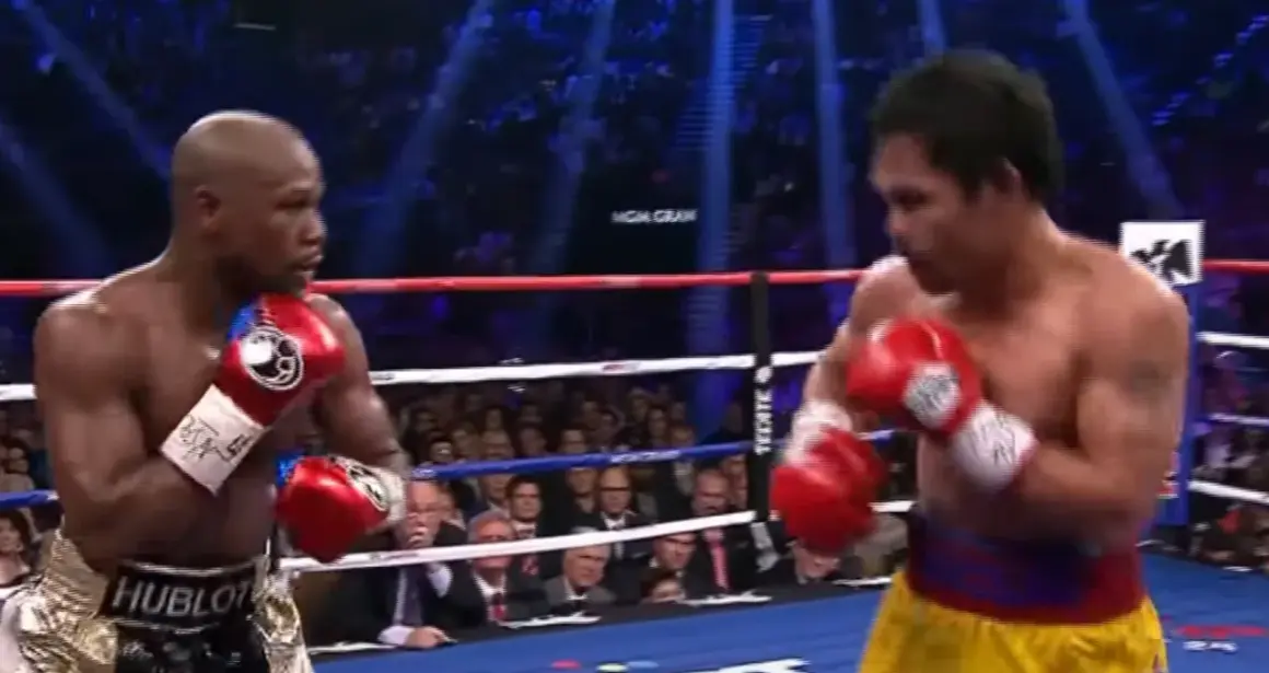 Floyd Mayweather Jr. in his signature defensive stance, hands up, ready to counter. His opponent, Manny Pacquiao, is in the foreground.