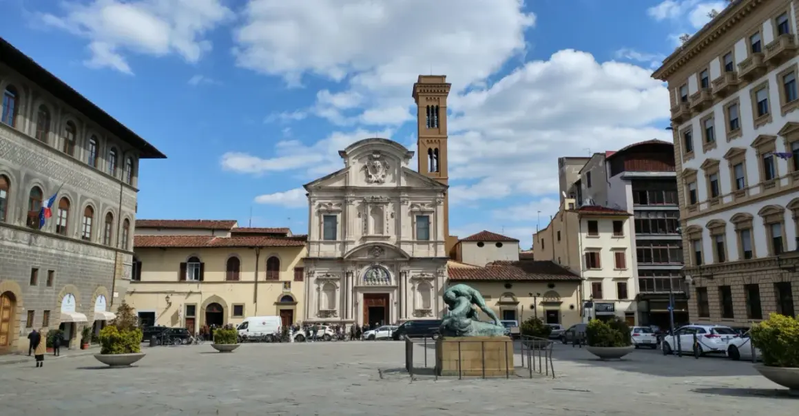 Piazza Ognissanti con la facciata della chiesa di San Salvatore in Ognissanti, una scultura al centro e palazzi circostanti.