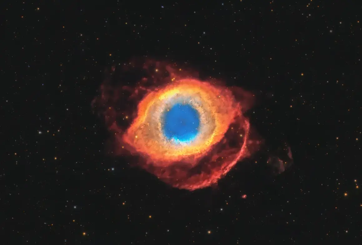 Helixnebulosan, ett kosmiskt öga av gas och stoft, lyser i rött och blått mot en stjärnbeströdd rymd.