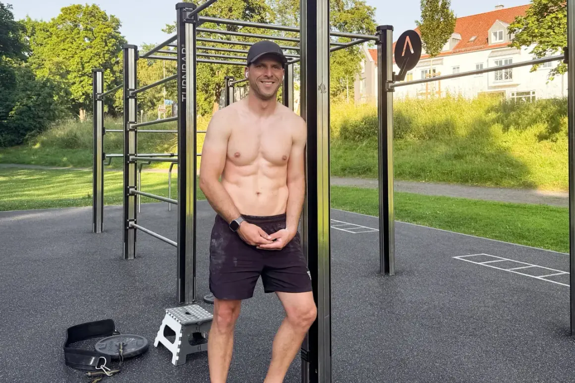 Ein trainierter Mann steht lächelnd vor einer Calisthenics-Anlage im Freien.