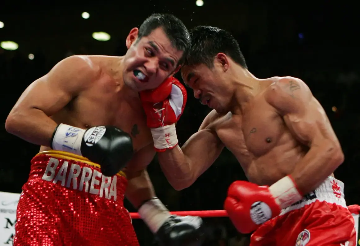 A boxer wearing red shorts with "BARRERA" emblazoned on them takes a hit.