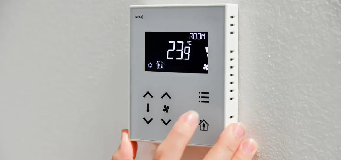 Dłoń dotyka panelu sterownika do powietrznej pompy ciepła, wyświetlającego 23.9°C.
