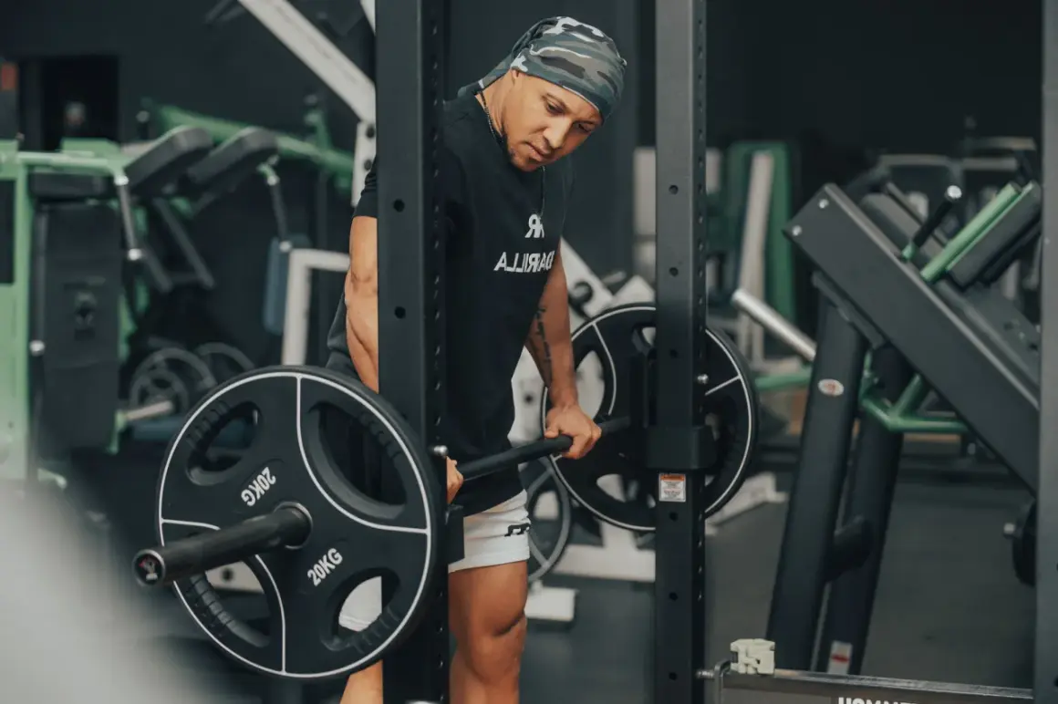 Mann mit Bandana macht schwere myo reps mit Langhantel im Fitnessstudio.