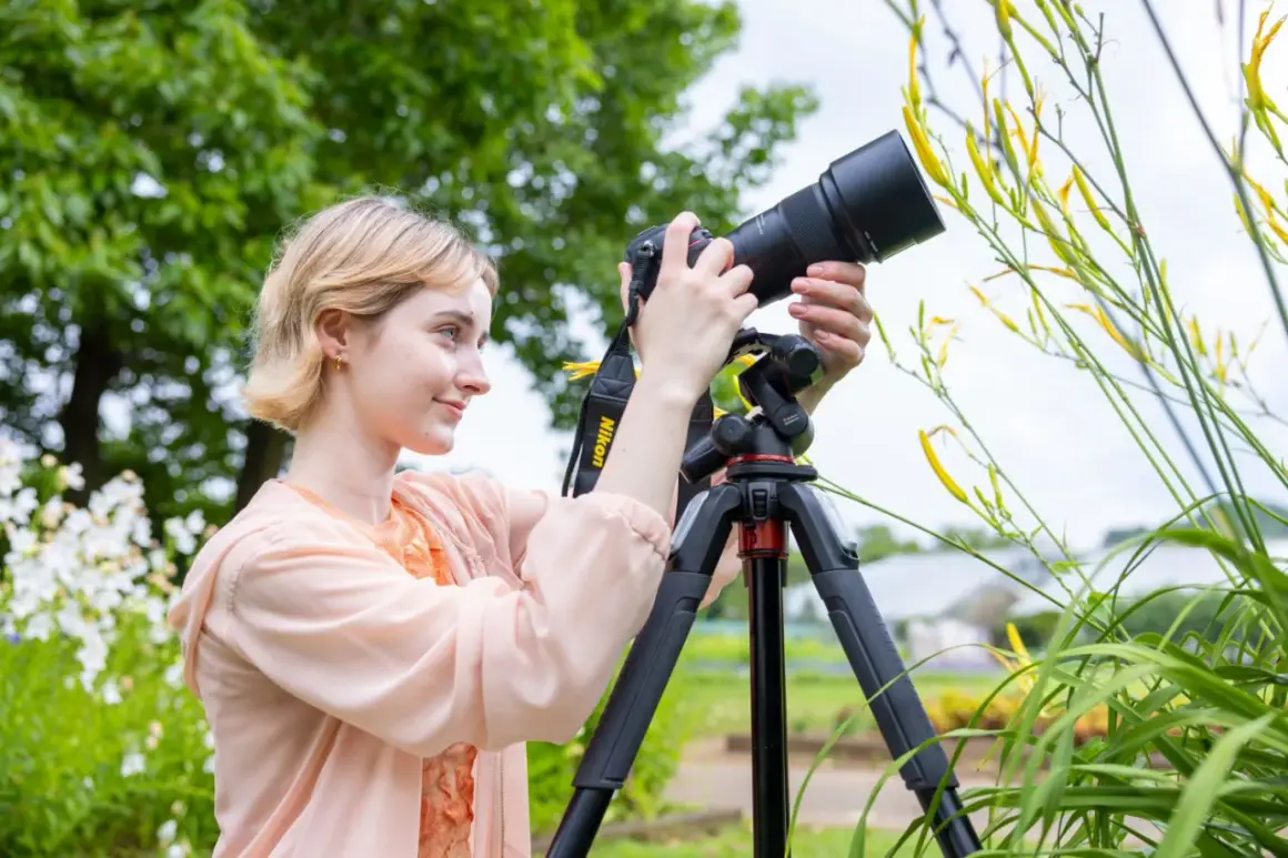 Kobieta z aparatem na statywie fotografuje żółte kwiaty w ogrodzie.