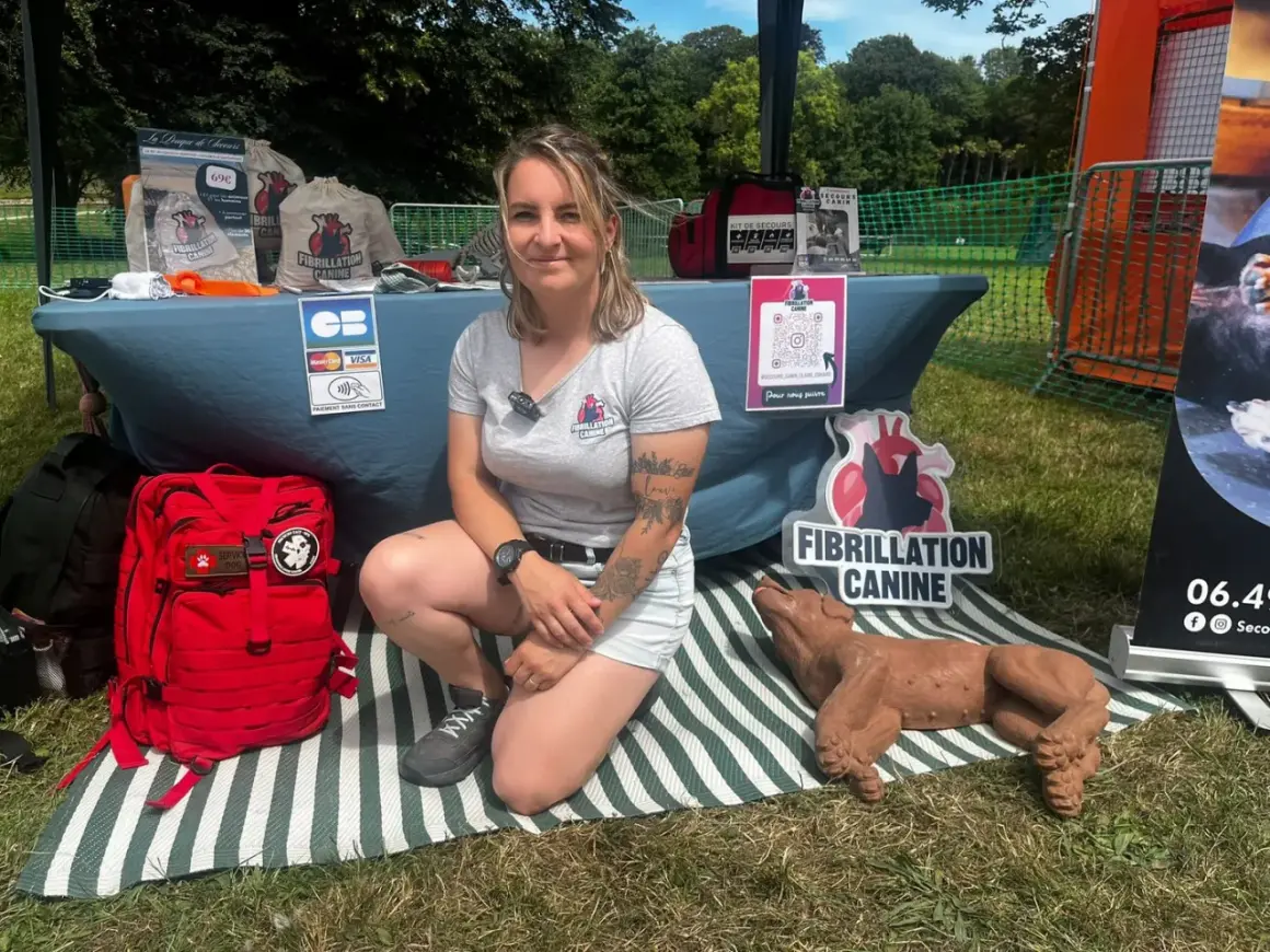 Une femme présente un stand sur la fibrillation canine, avec un mannequin de chien et du matériel de premiers secours. Elle enseigne le massage cardiaque chien.