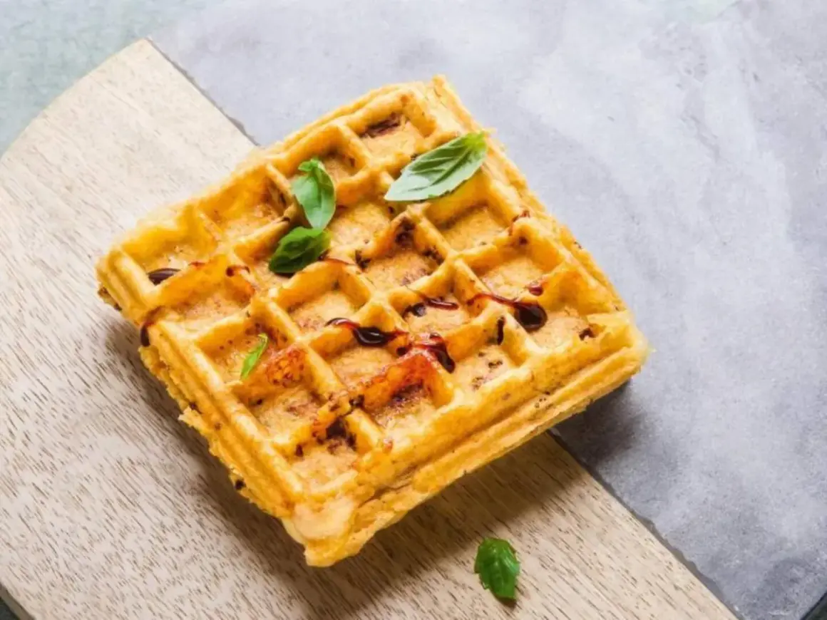 Goldbraune belgische Waffeln mit dunklem Sirup und frischem Basilikum, serviert auf einem Holzbrett.