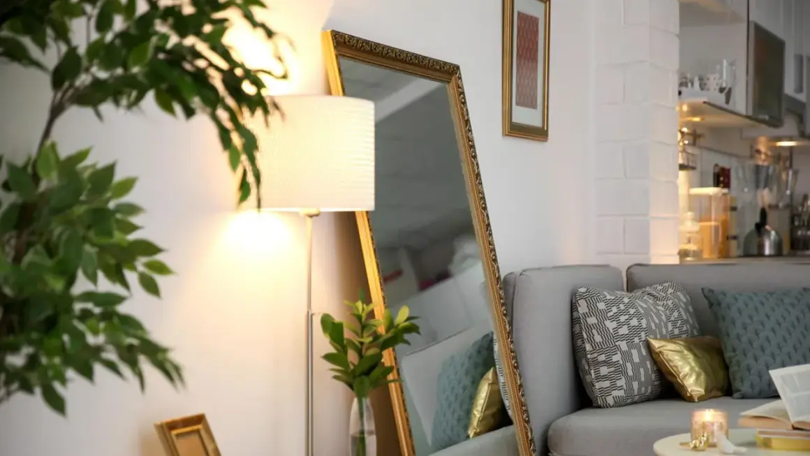 Ein großer Spiegel und eine Stehlampe helfen, die dunkle Wohnung heller zu machen. Ein Sofa mit Kissen und eine Pflanze vervollständigen die Szene.