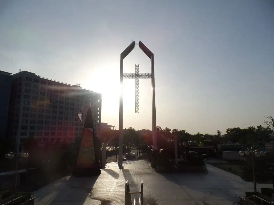 Ein monumentales Kreuz ragt im Gegenlicht empor, ein Symbol der Hoffnung, das mit dem Erbe von David Yonggi Cho verbunden ist.