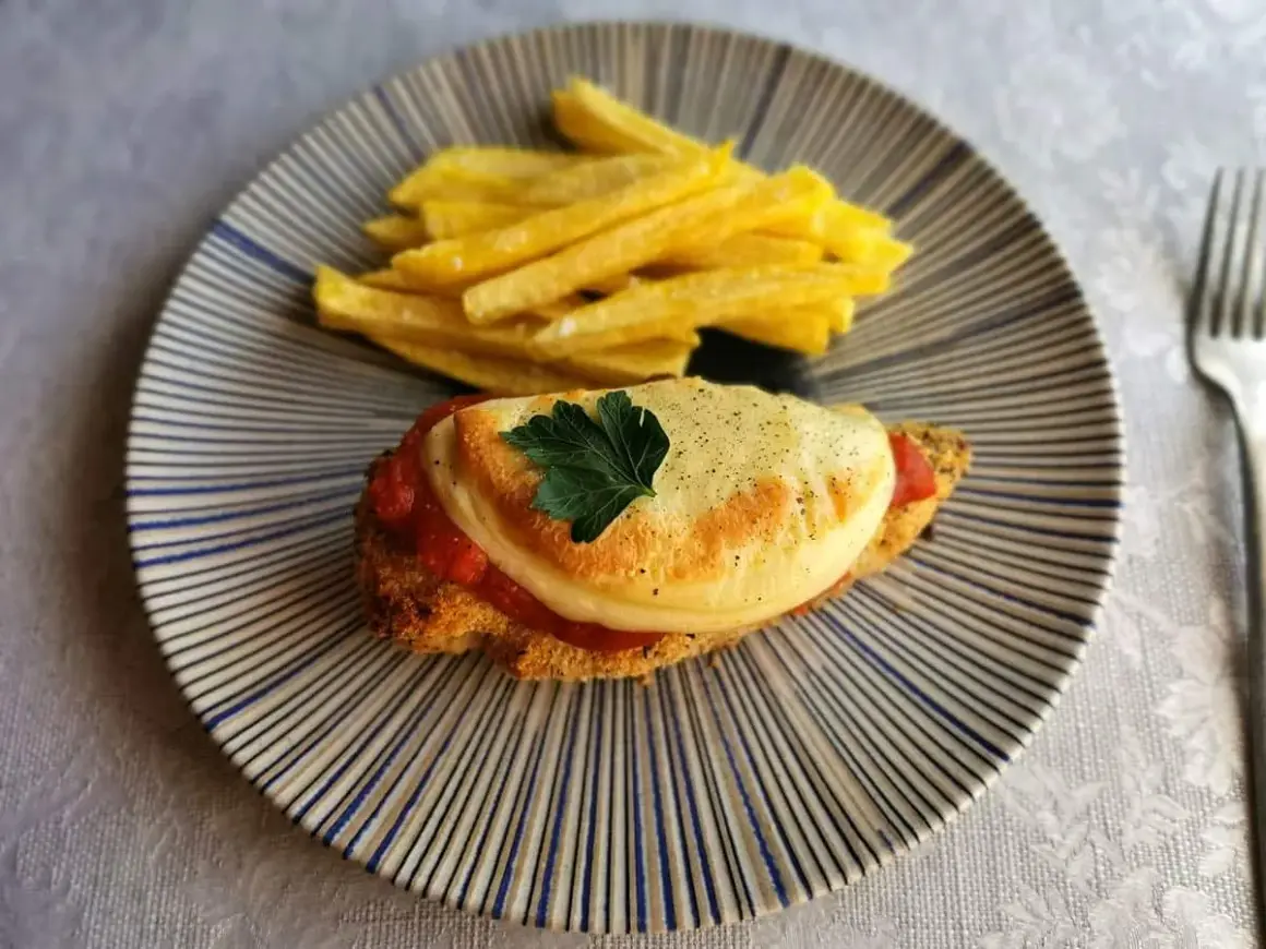 Delicioso pollo a la parmesana con papas fritas crujientes, servido en un plato rayado.