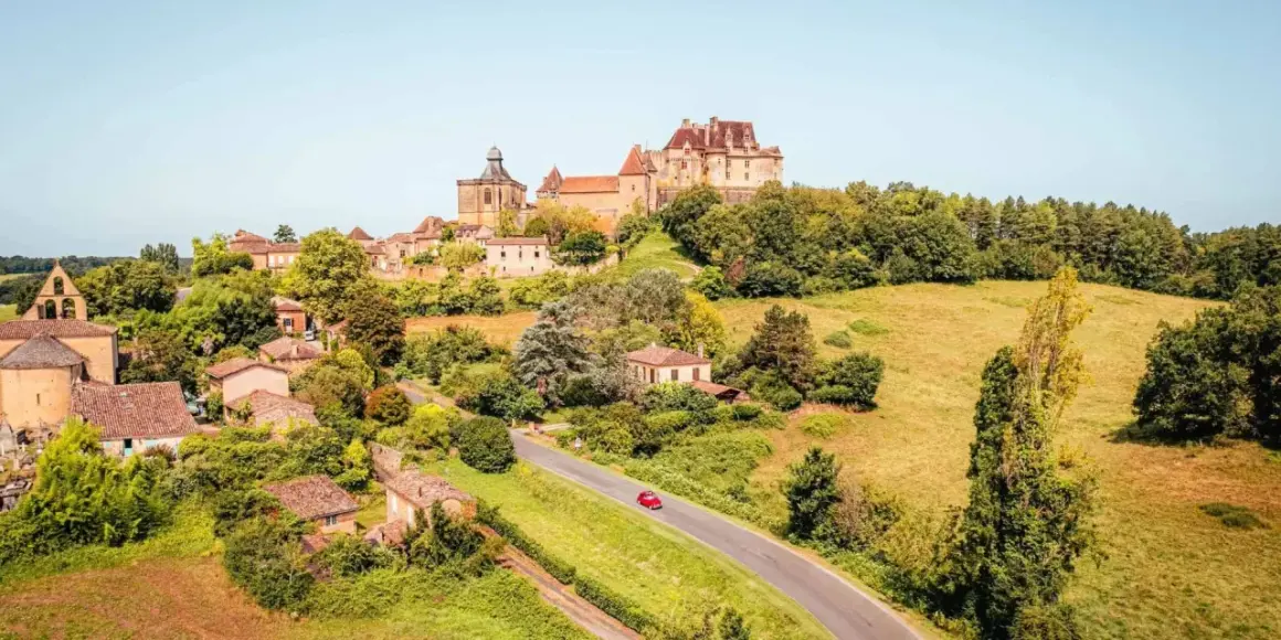 Un village pittoresque en France, idéal pour savoir où partir en France en mai. Un château domine la colline verdoyante.