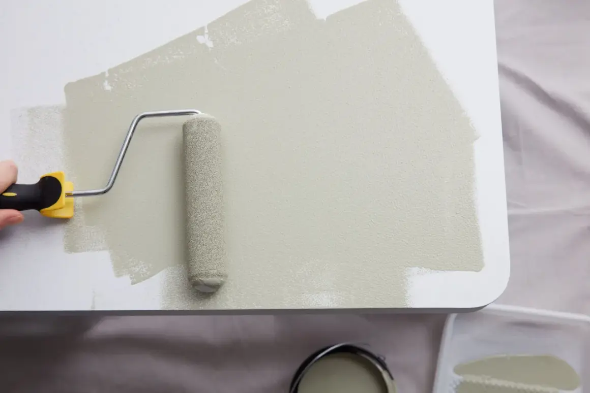 Application d'une peinture beige sur du mélaminé blanc avec un rouleau. Le résultat est une surface lisse et uniforme.