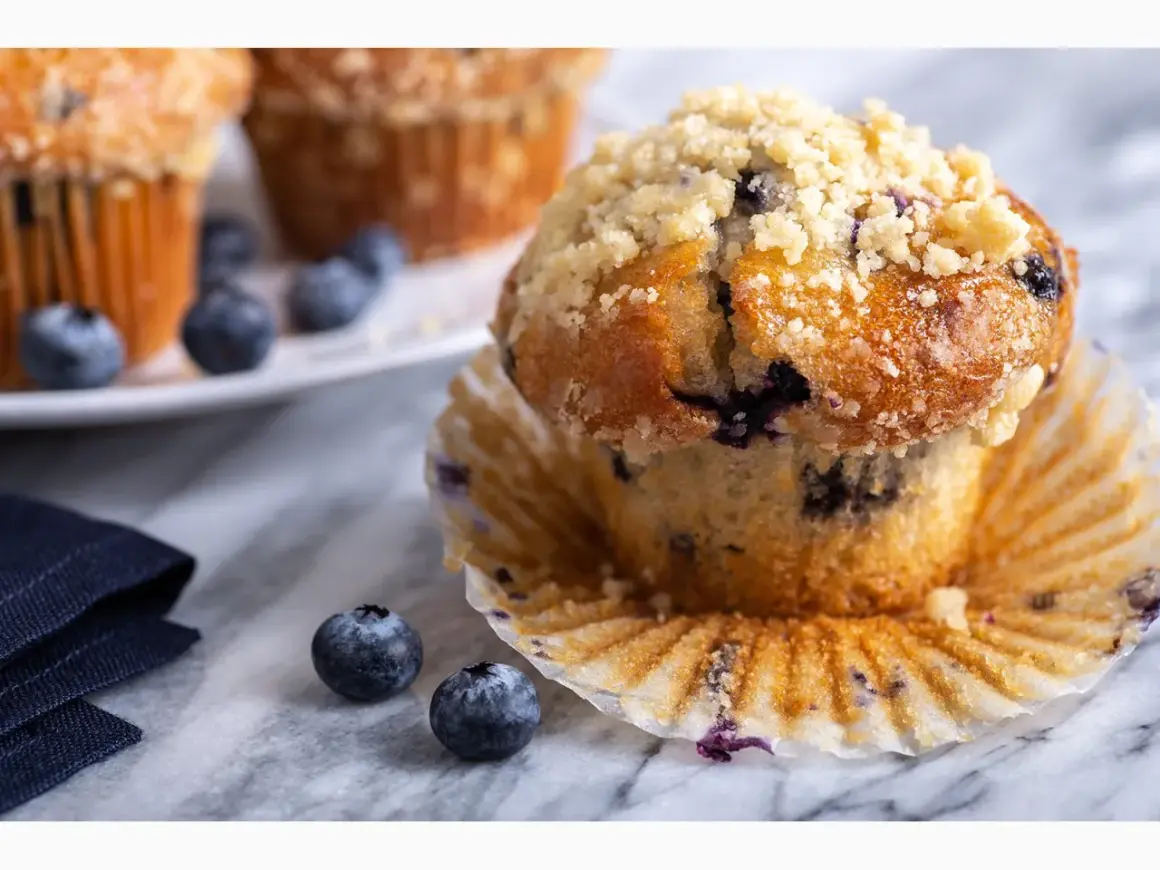 Saftige Blaubeermuffins mit Streuseln, perfekt für ein Blaubeermuffins Rezept. Frische Blaubeeren liegen daneben.